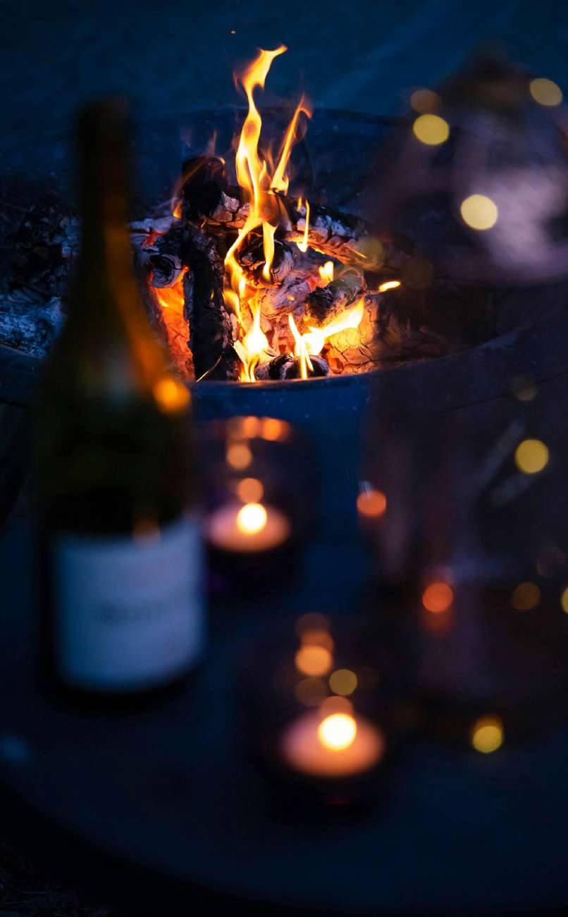 Velas acesas, fogo e uma garrafa de vinho ao anoitecer